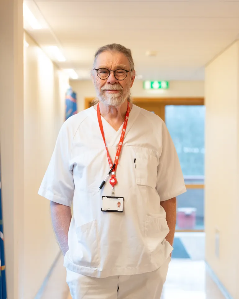 Mann i sykepleieruniform smiler mot kamera