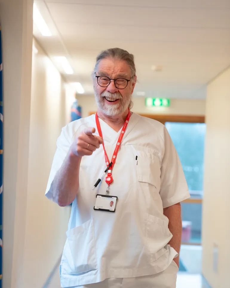 Mann i sykepleieruniform smiler og peker mot kamera