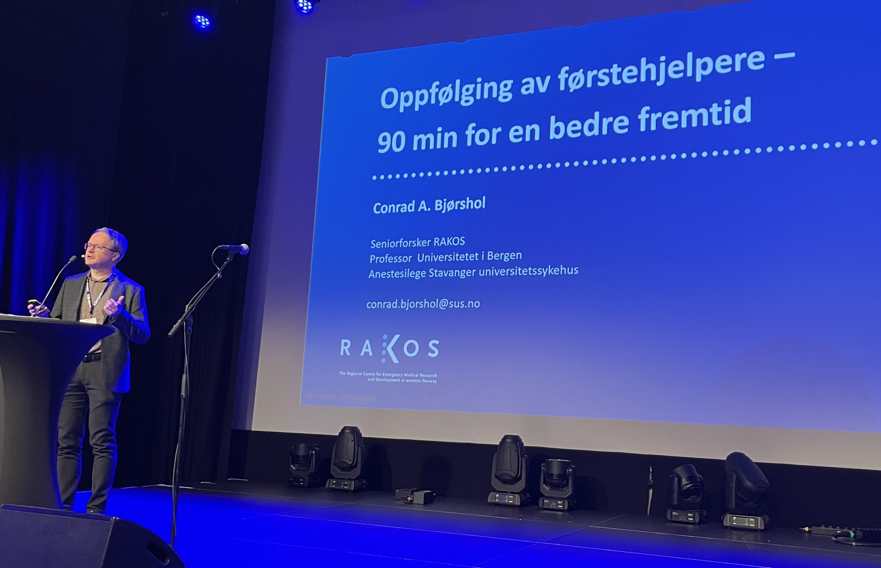 En person på en scene med mikrofon og skjerm bak seg