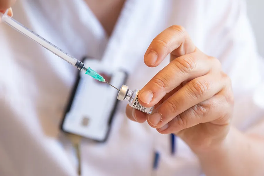 En person som holder en sprøyte og vaksineglass
