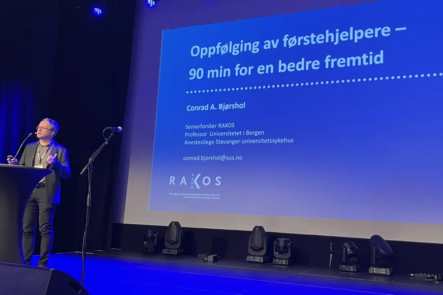 En person på en scene med mikrofon og skjerm bak seg