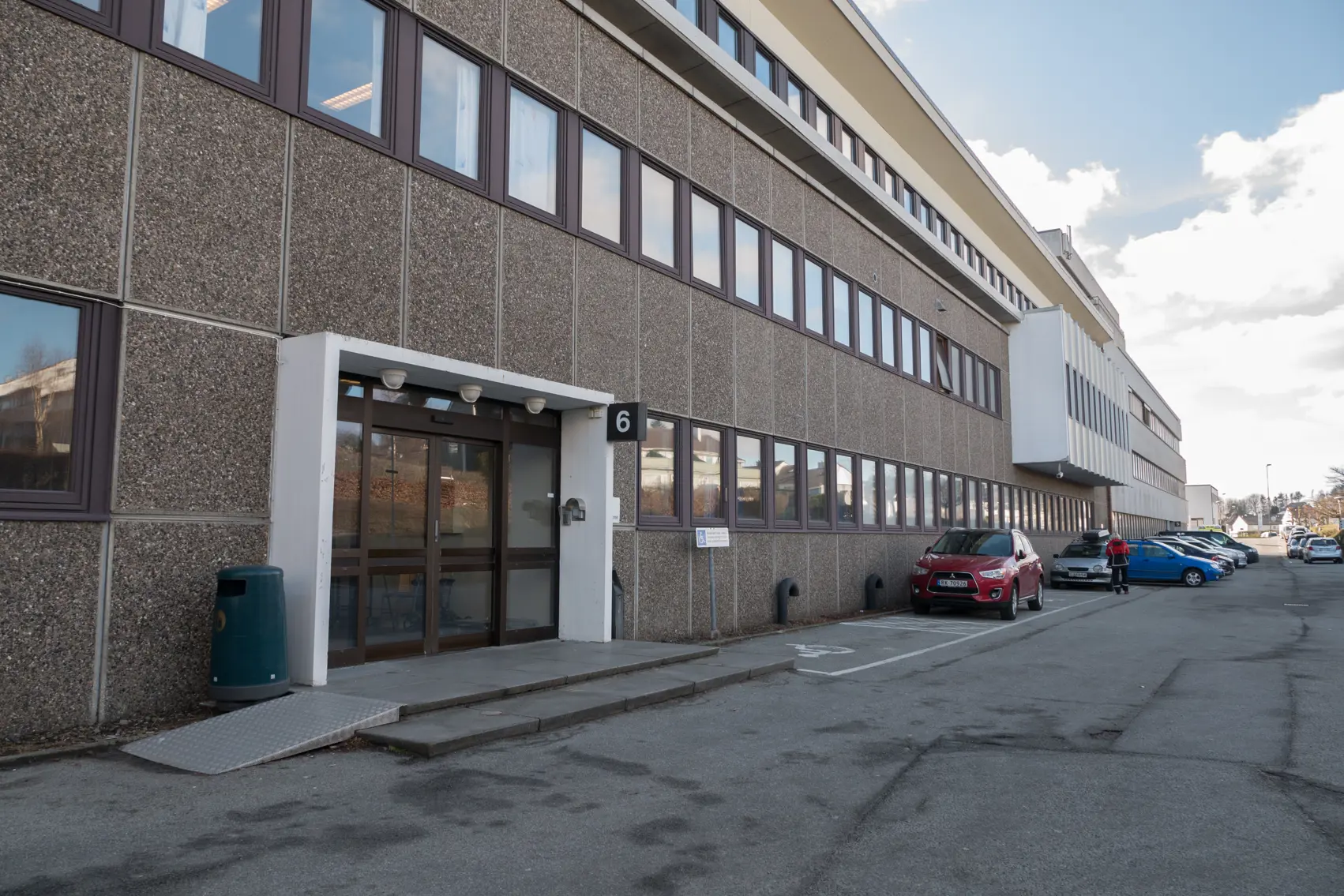 Et bygg med hovedinngang. Biler står parkert langs veggen.