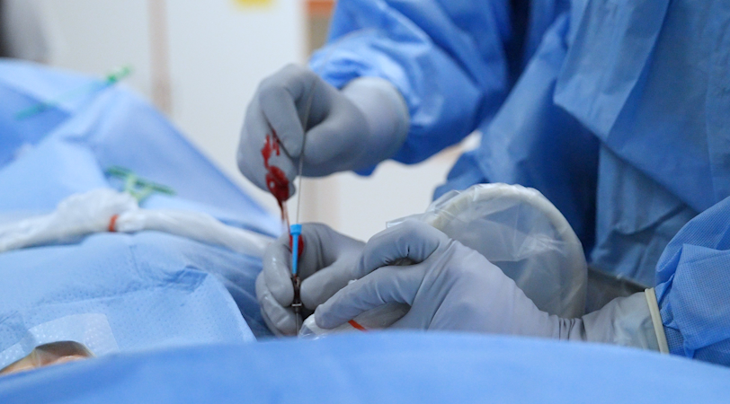 En person i kirurgisk skrubb og hansker som holder en sprøyte