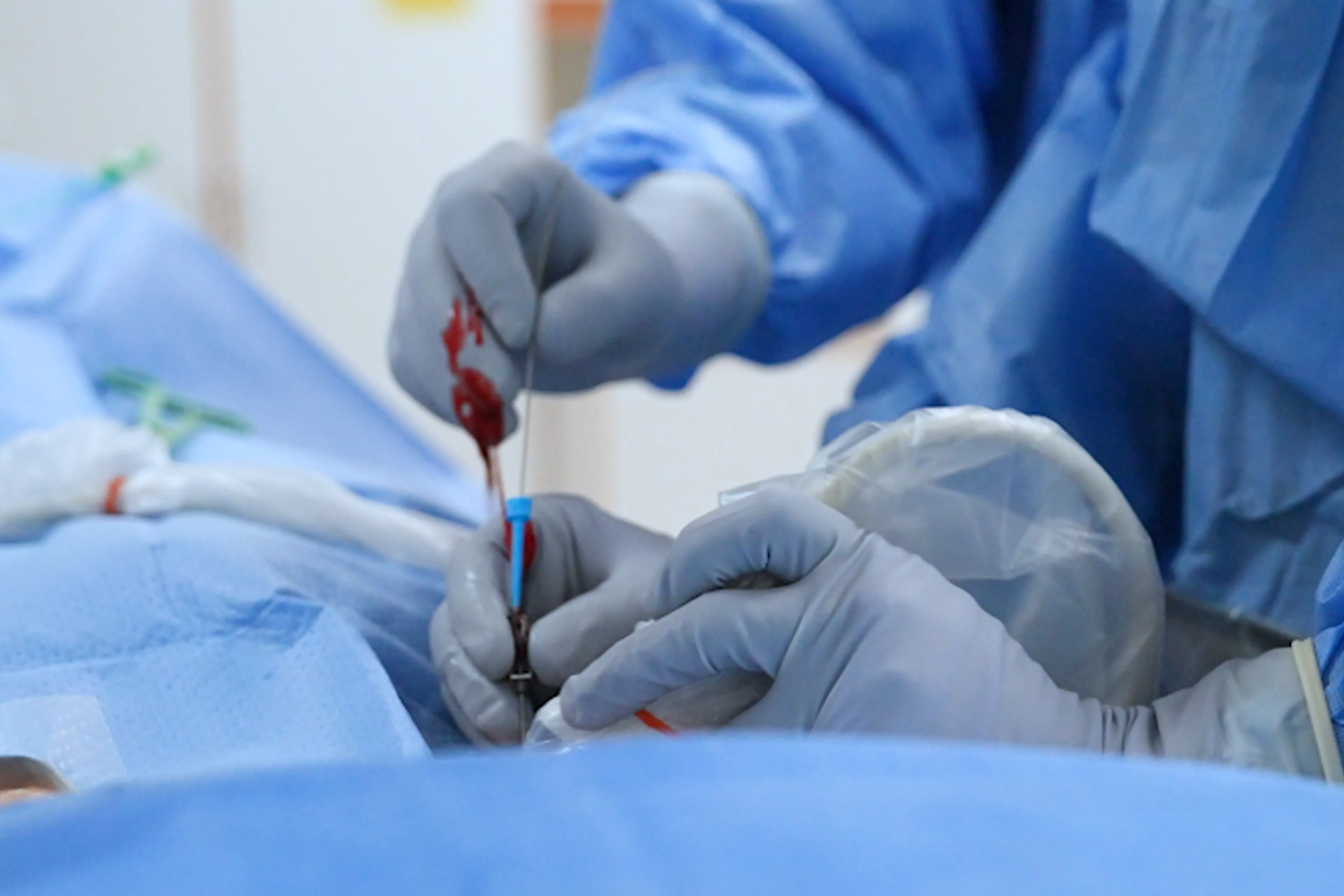 En person i kirurgisk skrubb og hansker som holder en sprøyte