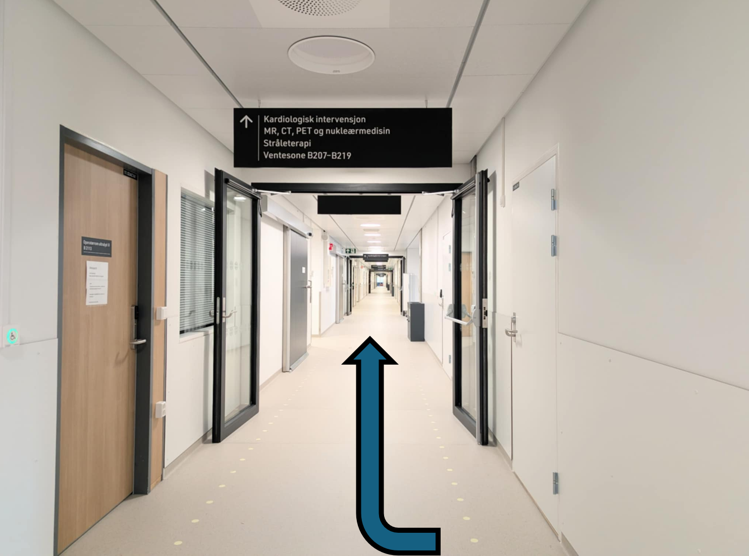 En lang korridor med dører og pil som viser vei
