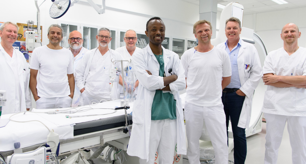 En gruppe mennesker i hvite labfrakker står ved siden av et hvitt bord