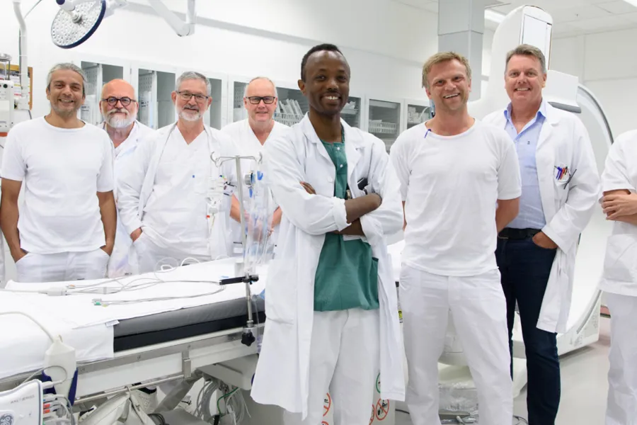 En gruppe mennesker i hvite labfrakker står ved siden av et hvitt bord