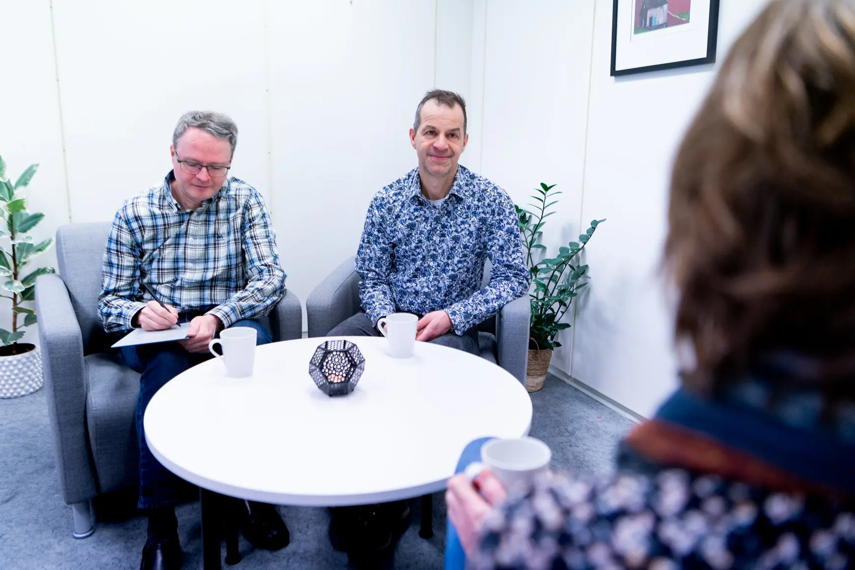 En gruppe menn som sitter rundt et bord med kopper og tallerkener