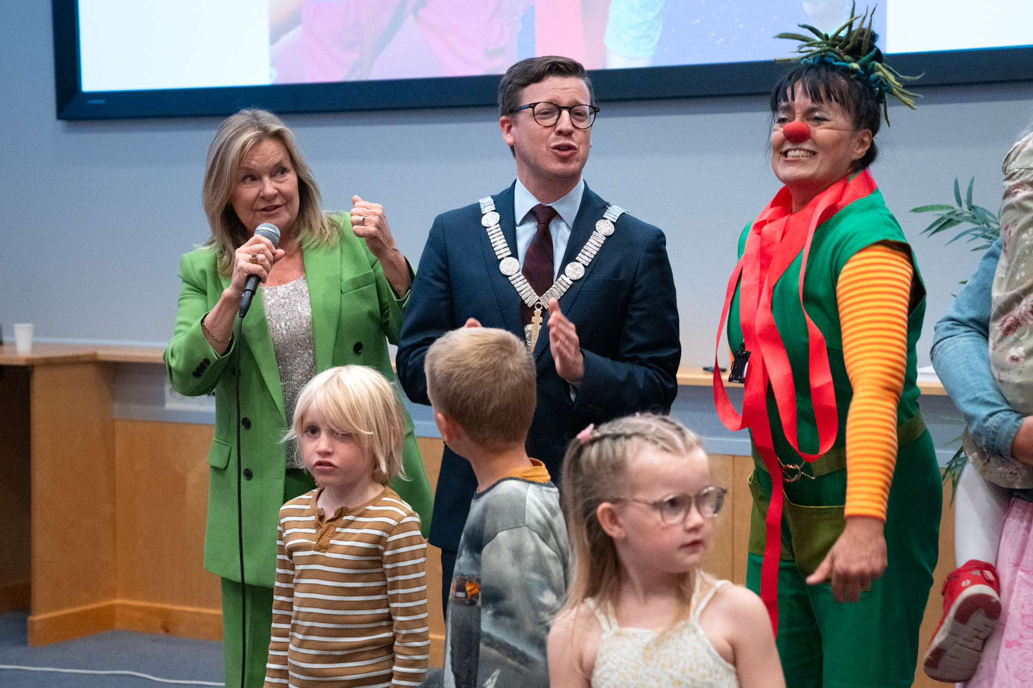 En person som snakker inn i en mikrofon med barn rundt seg