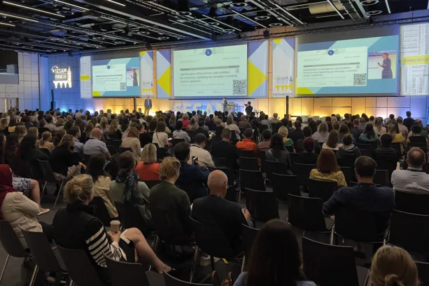 En gruppe mennesker som sitter i et rom med store skjermer