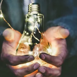 Hendler som holder en lyspære som lyser.