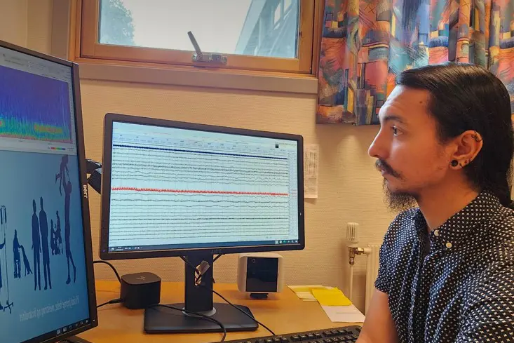 En person som sitter ved et skrivebord med en datamaskin og en skjerm