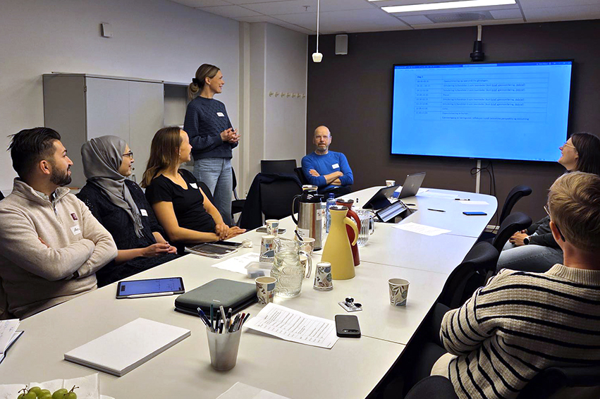 En gruppe mennesker som sitter rundt et bord med en projektorskjerm