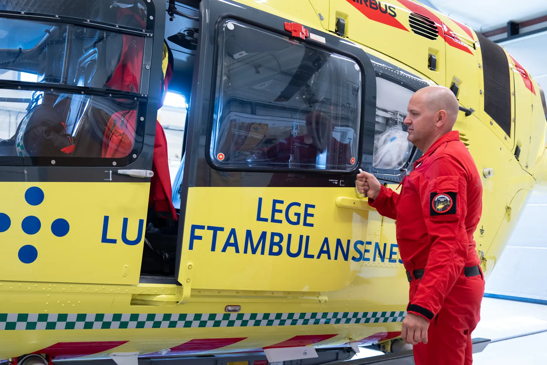 Mann i rød uniform står foran et gult ambulansehelikopter.
