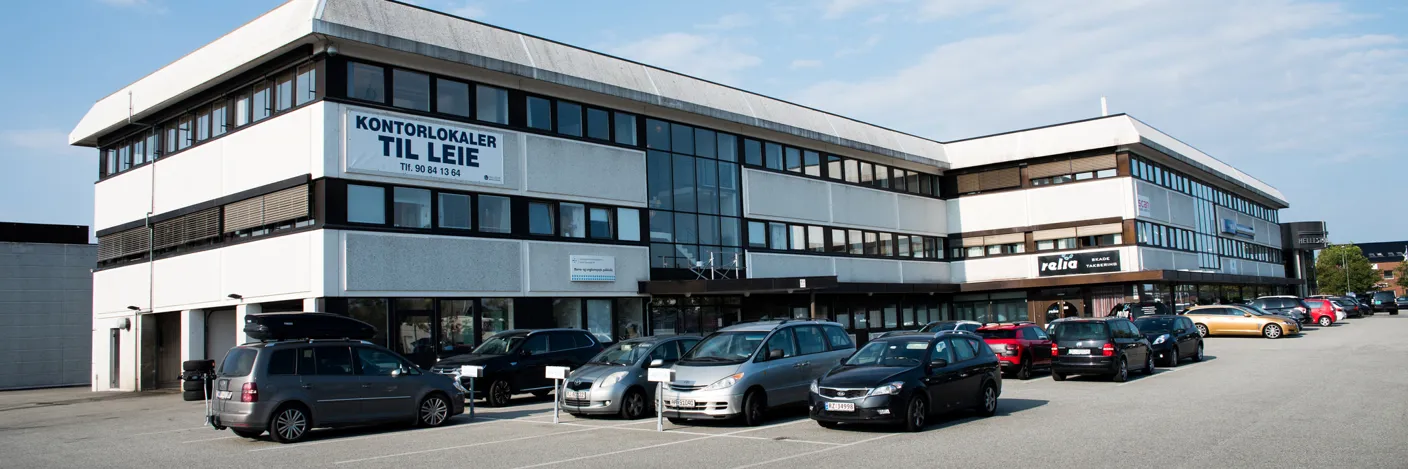 Hvitt, langt hus med parkeringsplass foran.