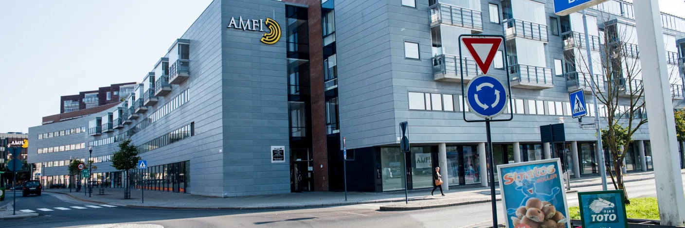 Grått bygg med vinduer og Amfi-skilt som ligger rett ved en rundkjøring.