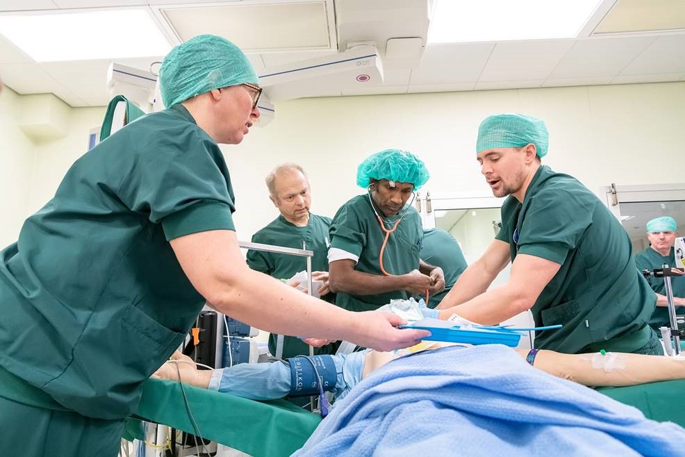 Simulering i akuttmottak. Tre helsepersonell står over en person som leker pasient. Foto.