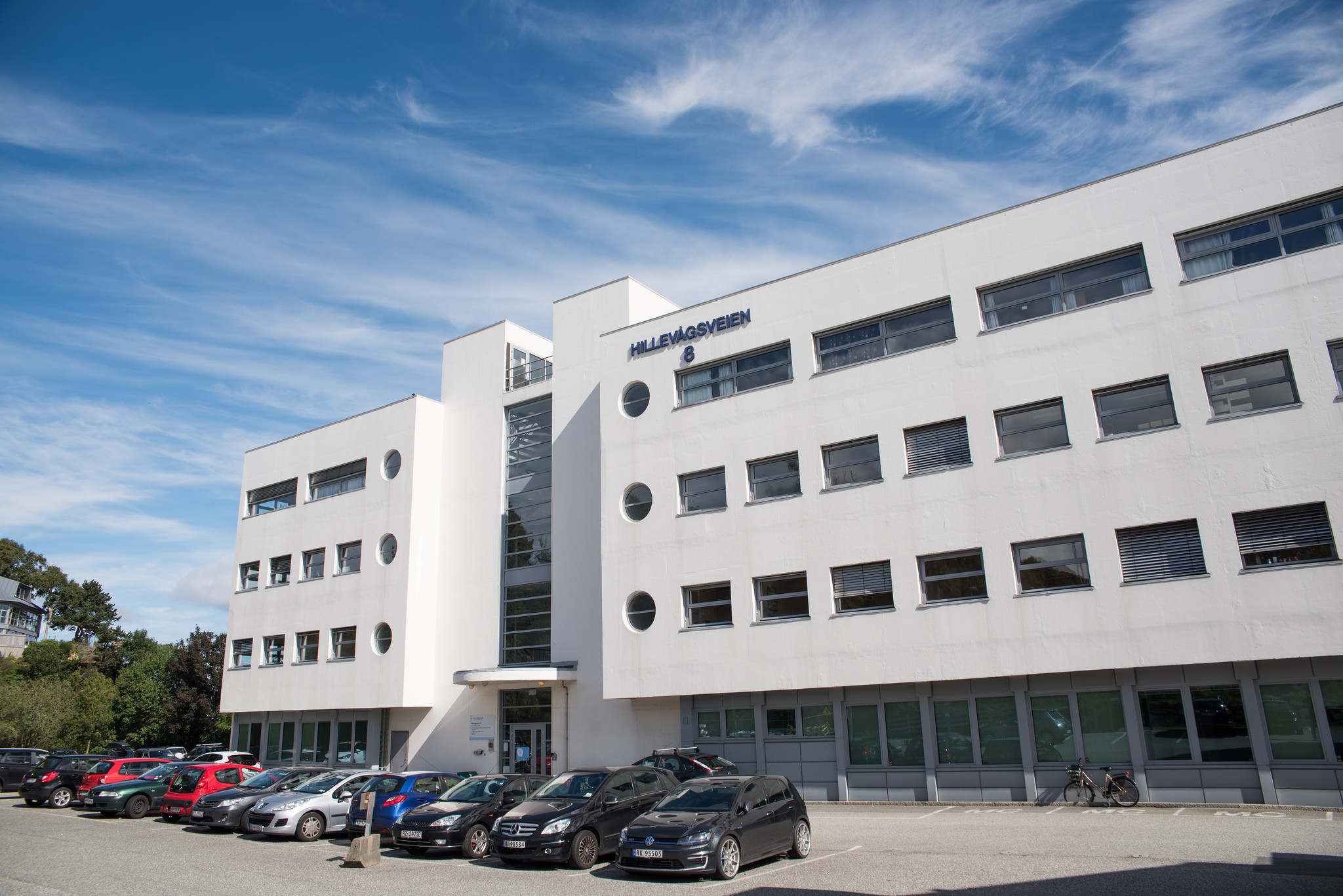 Hvitt murbygg med parkeringsplass foran.