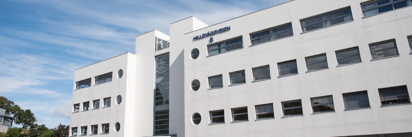 Hvitt murbygg med parkeringsplass foran.