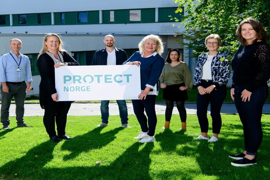 En gruppe med mennesker som holder opp et banner med PROTECT logo på