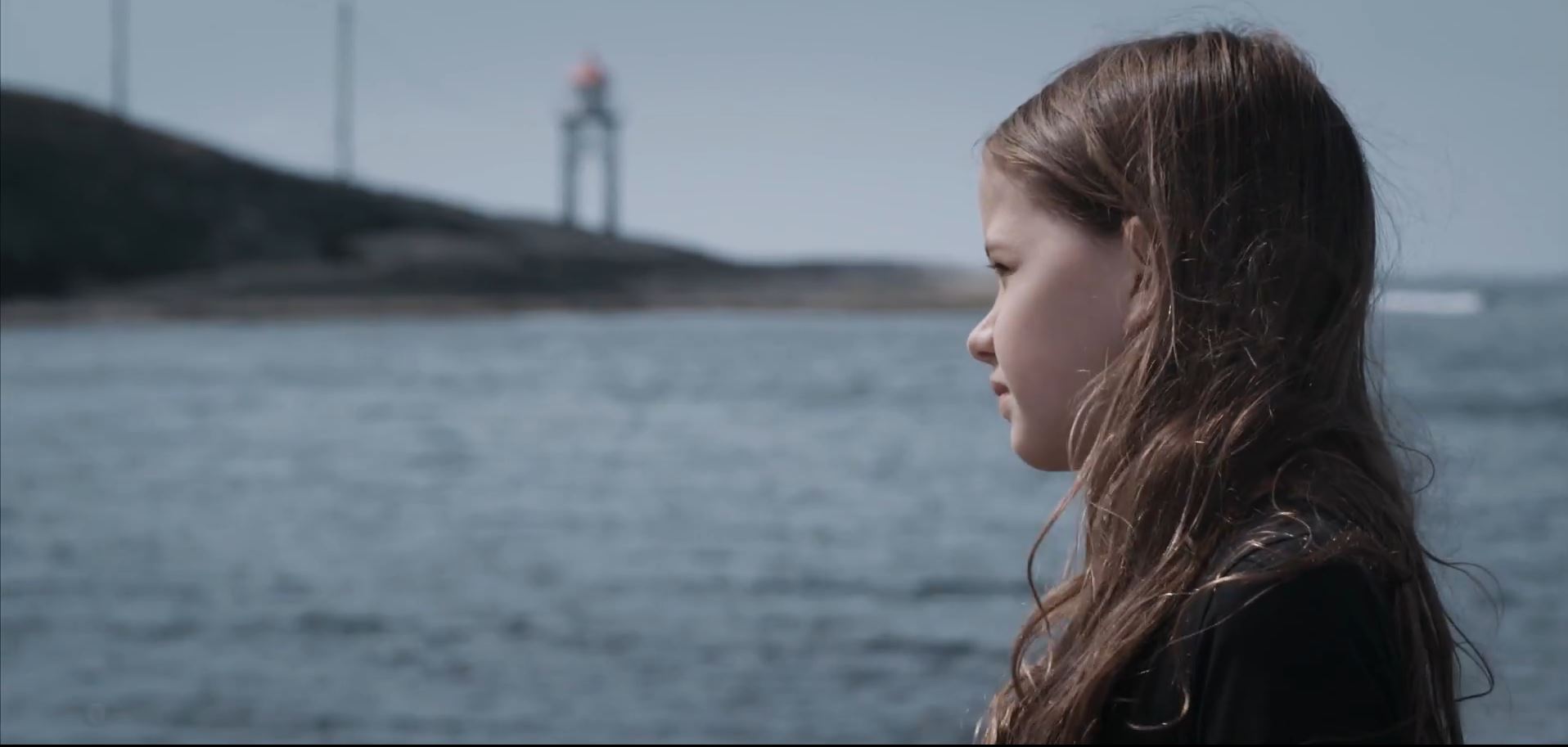 Ung jente står ved kysten og ser utover havet. Bilde.