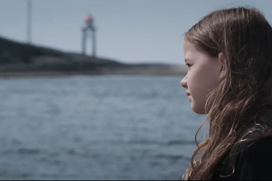 Ung jente står ved kysten og ser utover havet. Bilde.