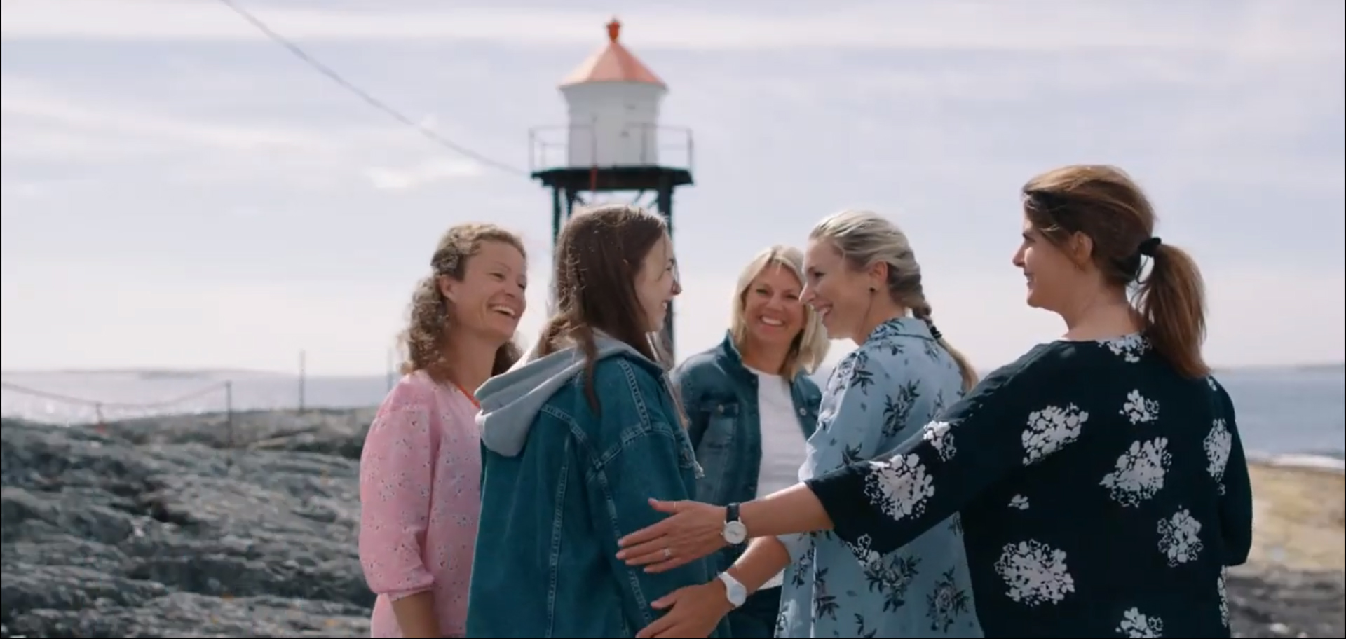 Voksne og en ungdom står ved et fyrtårn og smiler. Bilde.