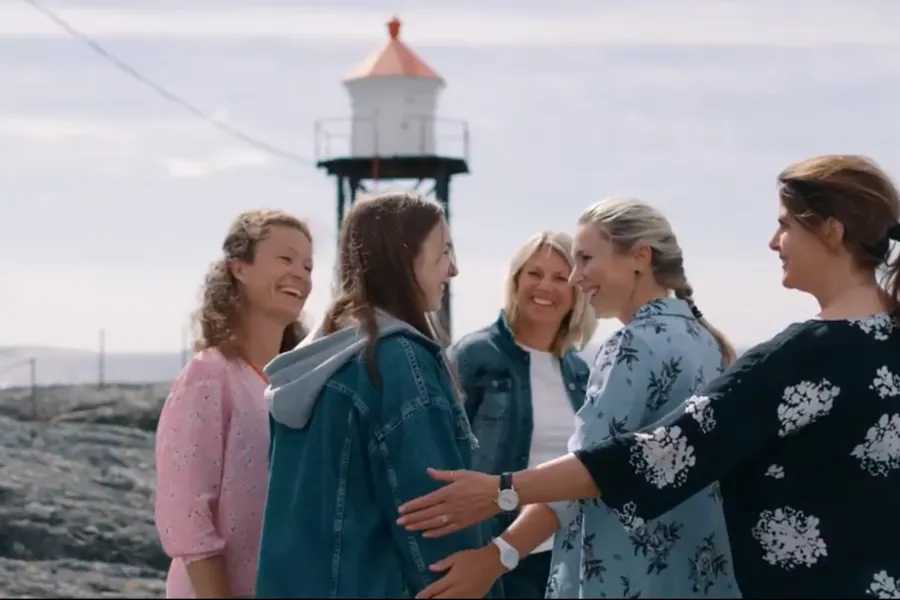 Voksne og en ungdom står ved et fyrtårn og smiler. Bilde.