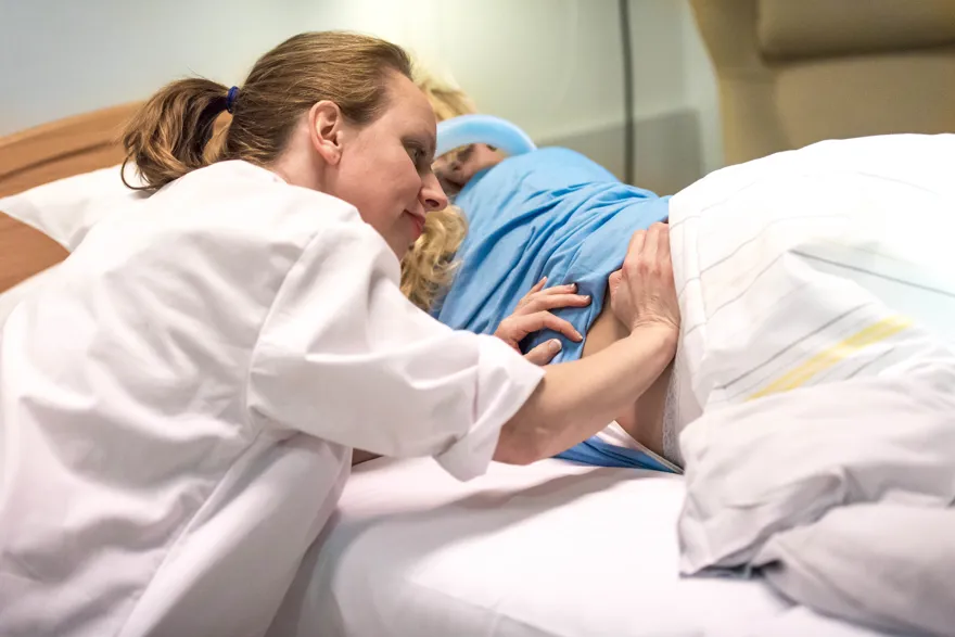Jordmor som masserer gravid kvinnes rygg. Foto.