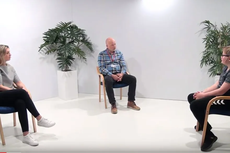 To medarbeidere i vanlige klær, og en tenåring som sitter på hver sin stol i studio. Bilde.