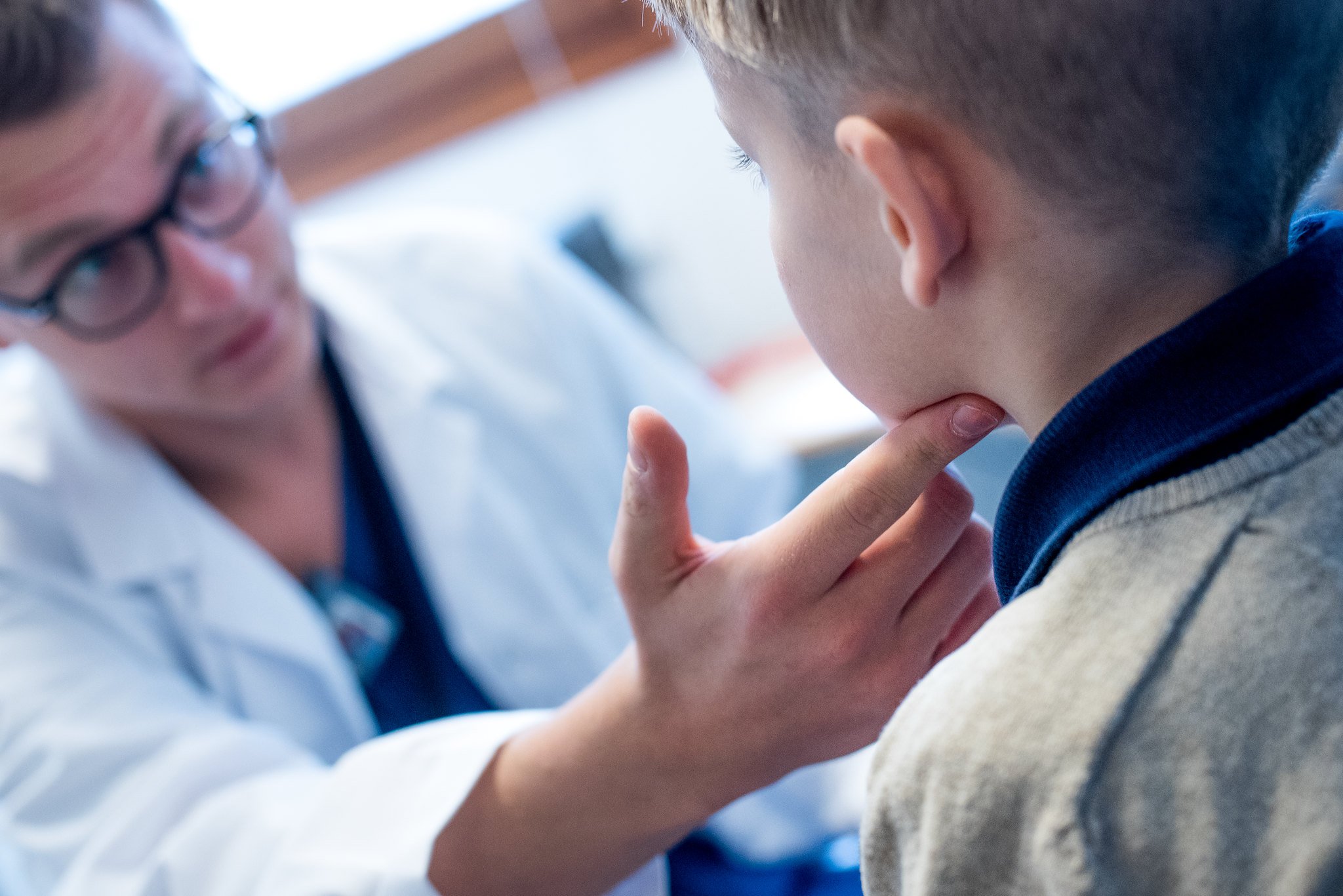 Lege som kjenner på halsen til et barn. Foto.