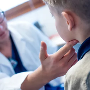 Lege som kjenner på halsen til et barn. Foto.