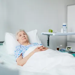 Eldre pasient ligger i en seng. Foto.