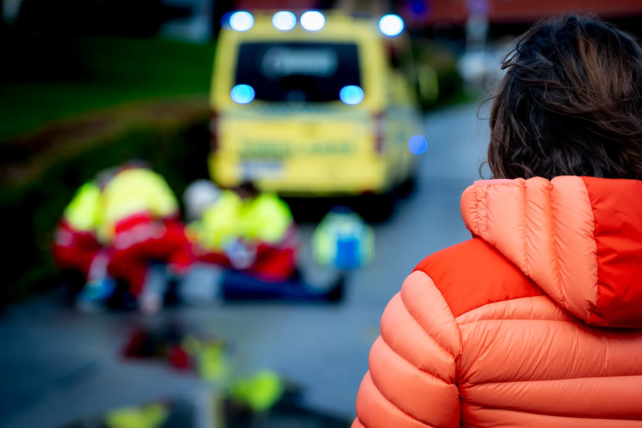 Ambulansepersonell gir førstehjelp til person på bakken. Kvinne står alene og ser på.