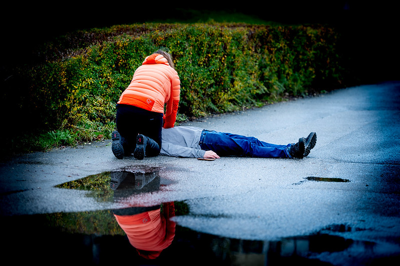 Kvinne sitter på kne forann person som ligger på bakken
