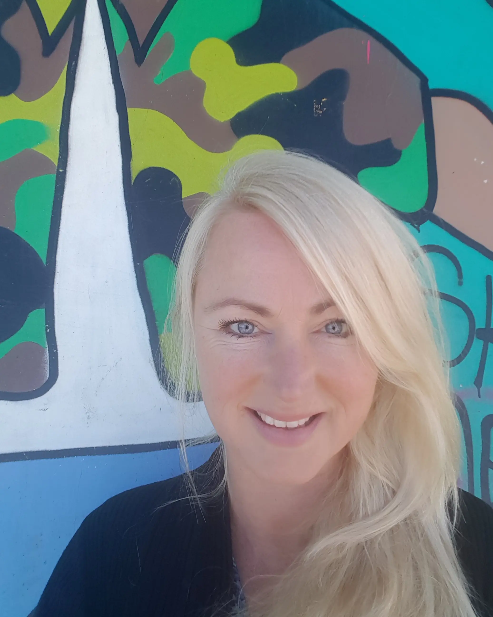 Kvinne med blondt hår står foran fargerik vegg.