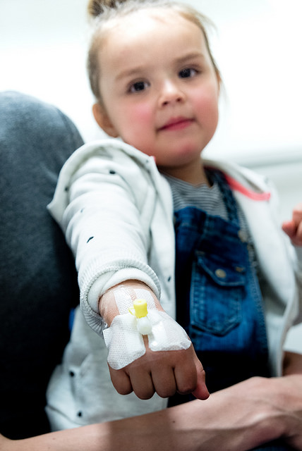 Barn som viser frem veneflon på hånden. Foto.