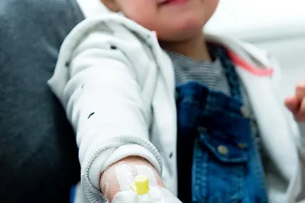 Barn som viser frem veneflon på hånden. Foto.