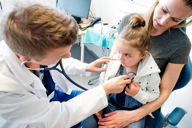 Barn på fanget til mor. Legen lytter på hjertet med stetoskop. Foto.