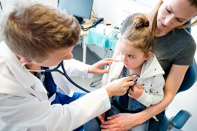 Barn på fanget til mor. Legen lytter på hjertet med stetoskop. Foto.