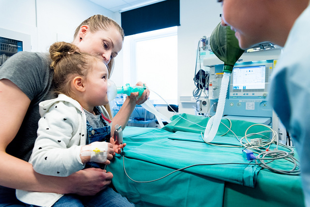 Barn på fanget til mor. Barnet får prøve en oksygenmaske. Foto.