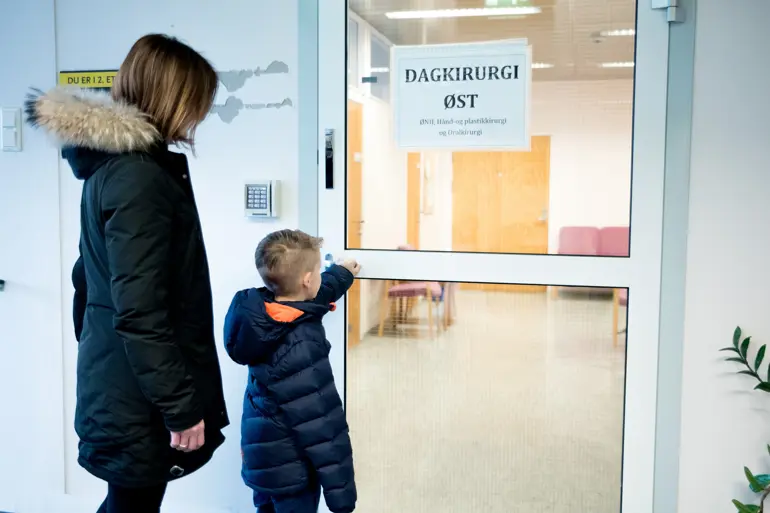 Mor og sønn står utenfor døren til dagkrirugi øst. Foto.