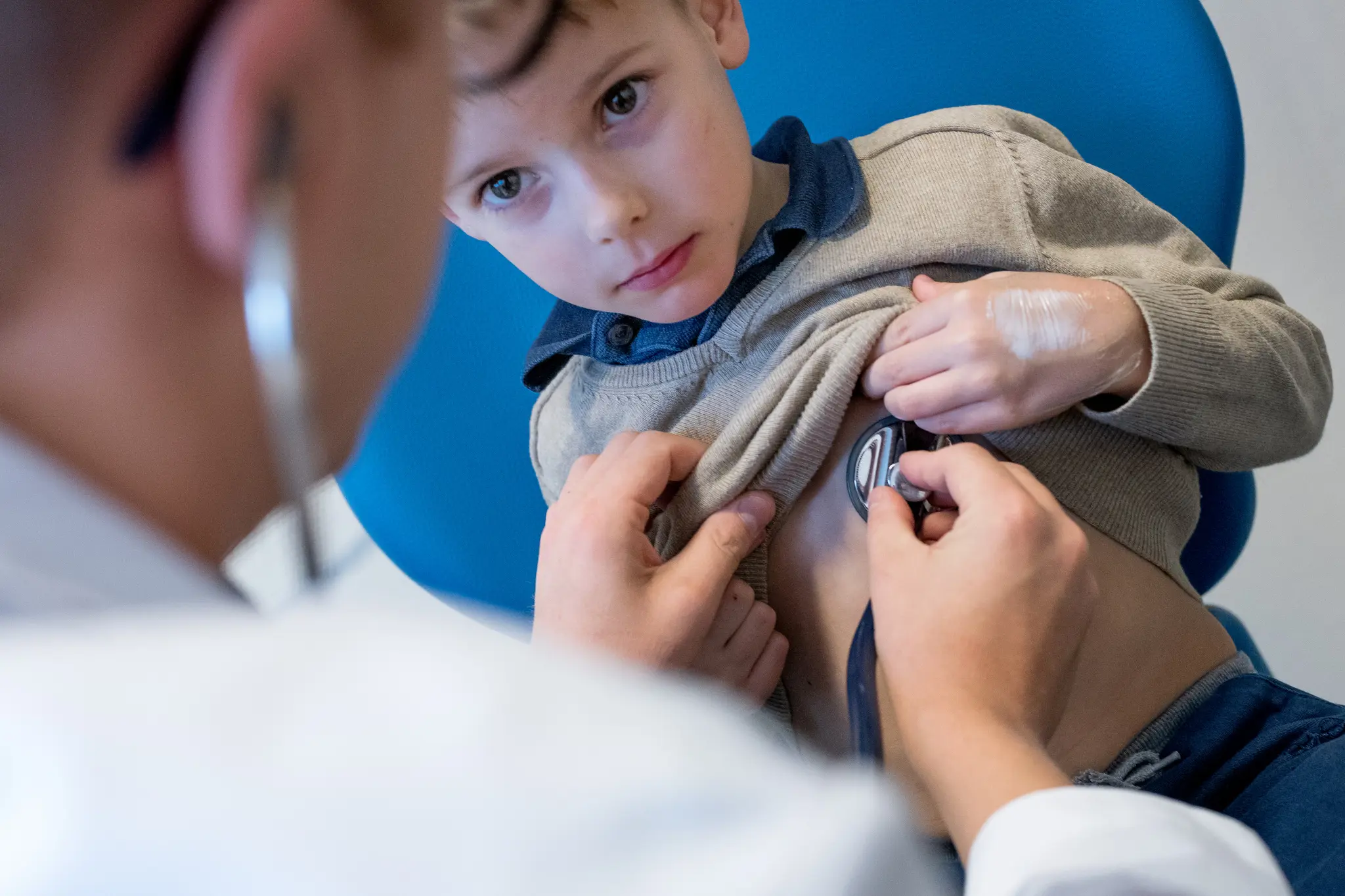 Liten gutt som ser på legen. Legen lytter på hjertet med et stetoskop. Foto.