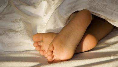 Et barn ligger under dynen i sengen med føttene stikkende ut