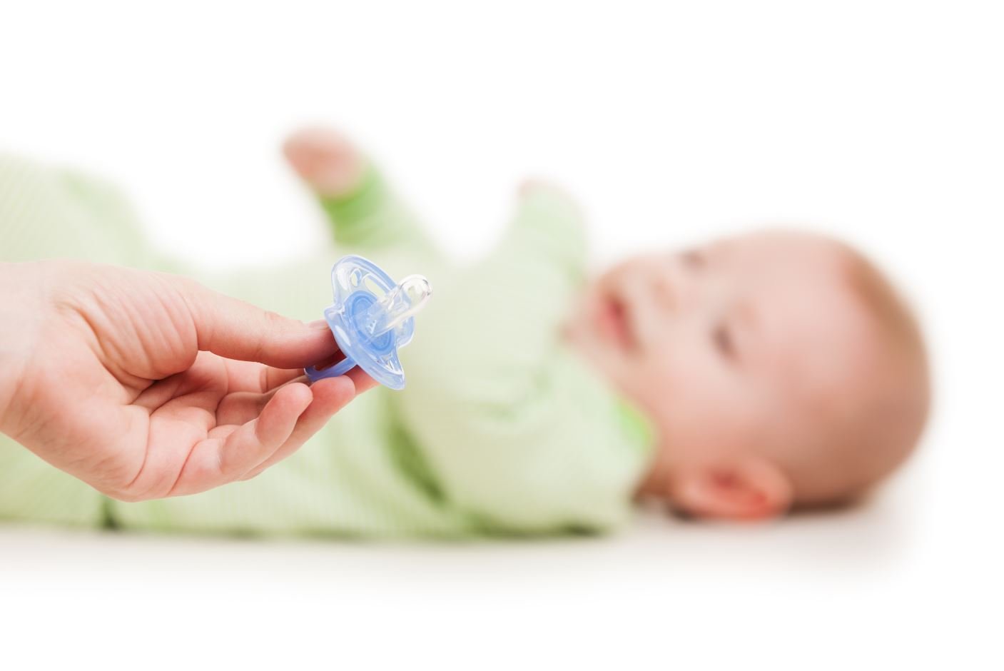 En voksen hånd holder ut en smokk foran ansiktet til et lite barn