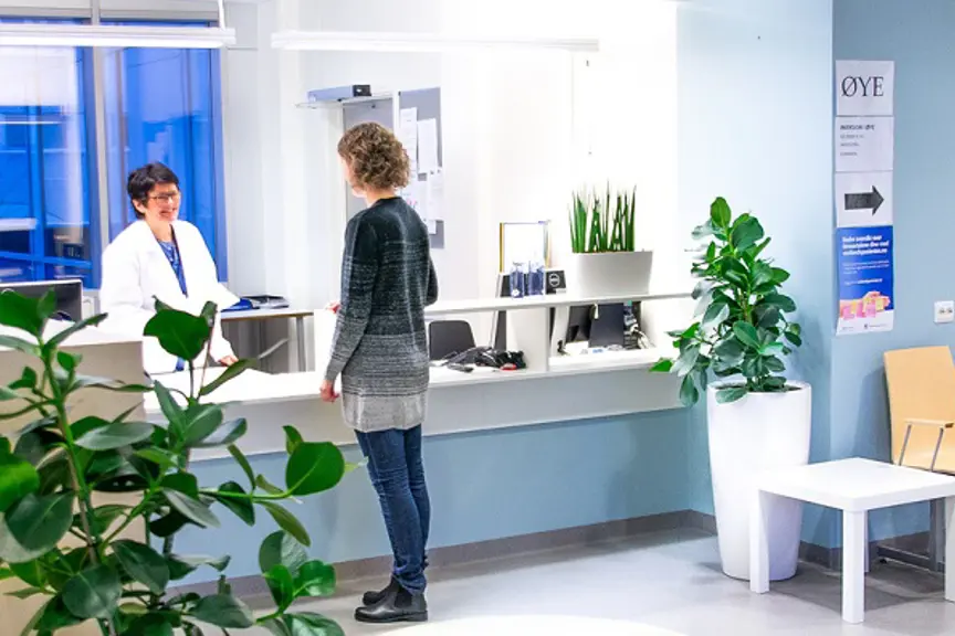 Pasient som står ved resepsjonen. Foto.