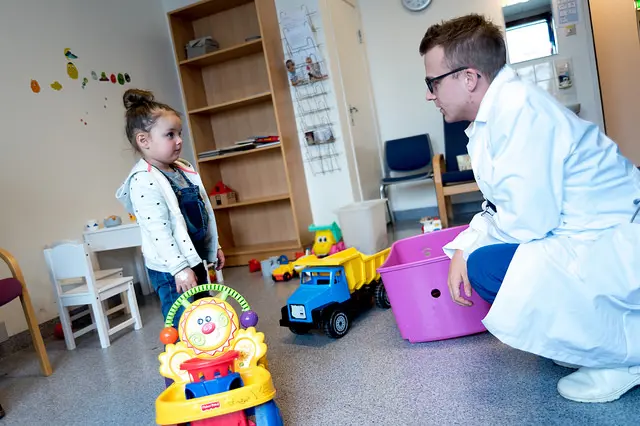Barn og lege på lekerommet. Legen sitter på huk. Foto.