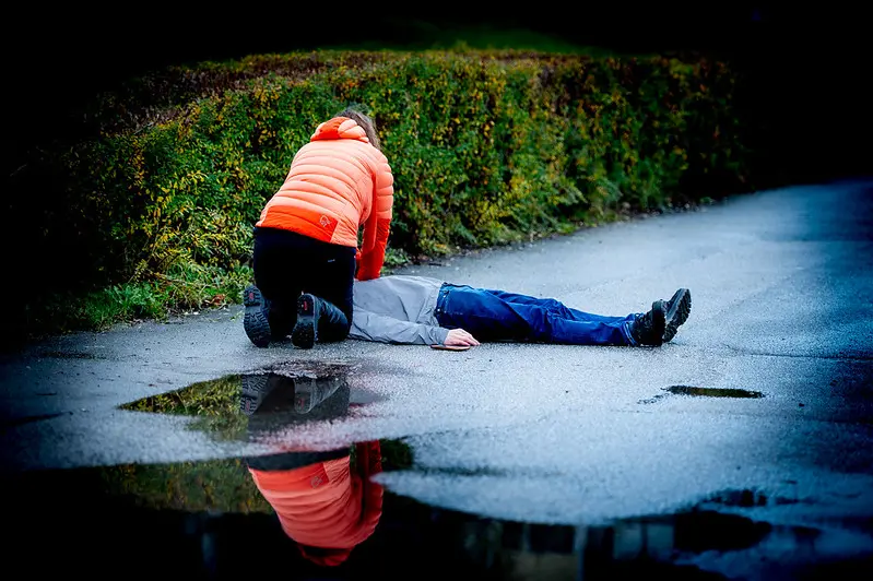 Kvinne bøyd over person som ligger på bakken