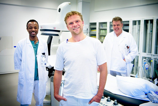 Tre hvitkledde menn står på en rekke og smiler inn i kamera.