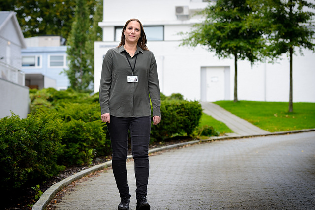 En kvinne står på brostein foran noen grønne trær